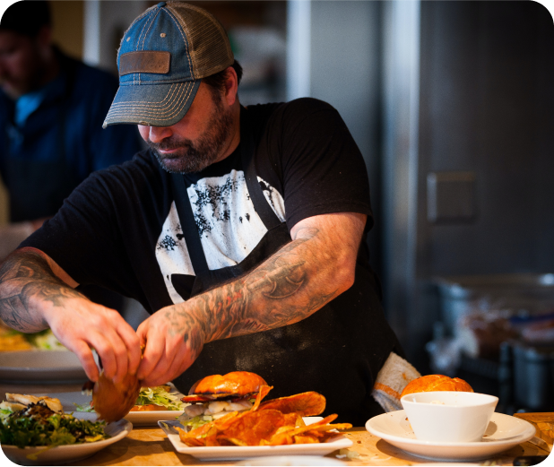 A chef is dressing a burger in the kitchen.
