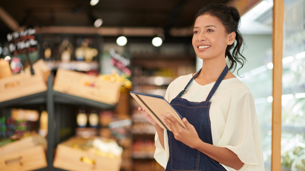 A female employee standing in the grocery store is holding a tablet.