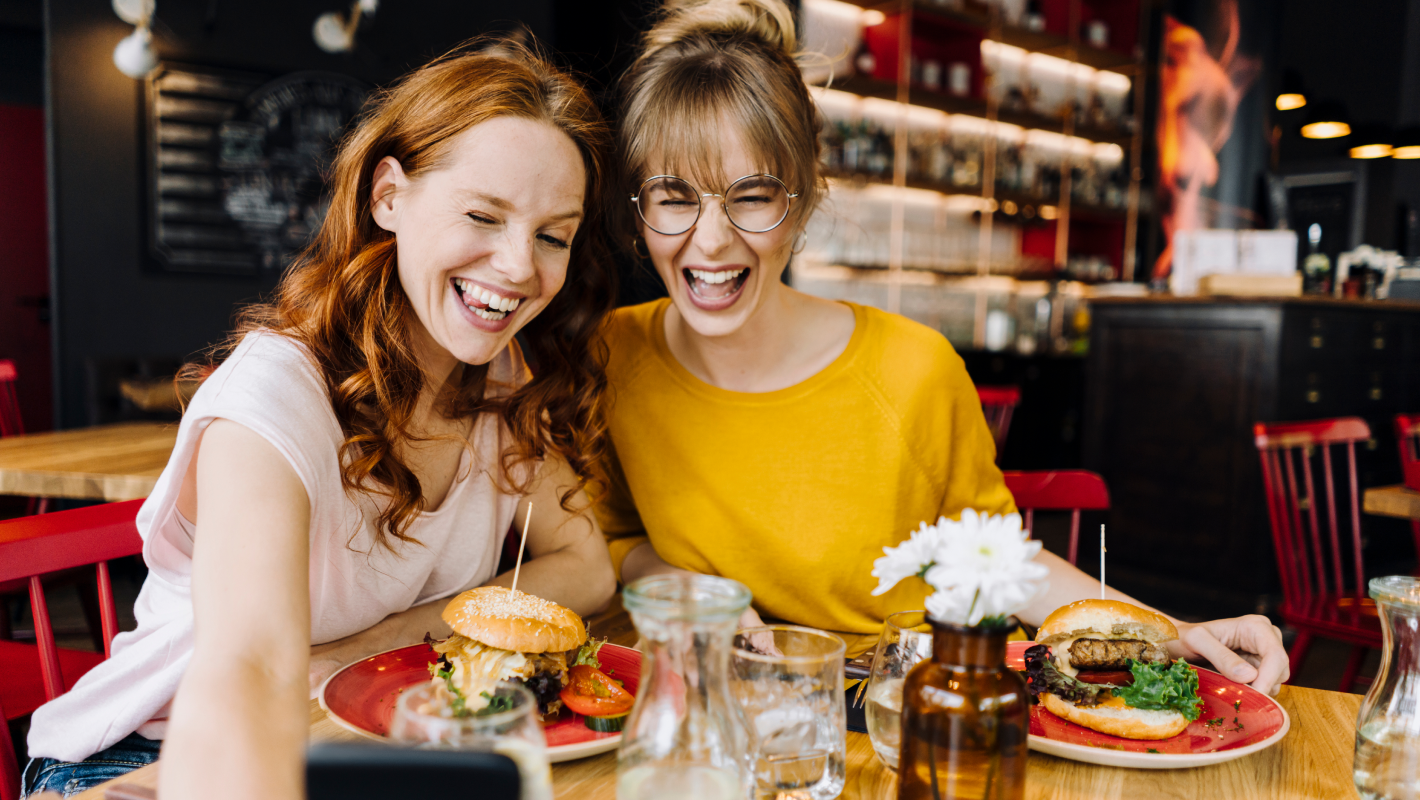 Two happy female friends having burger and taking selfie.