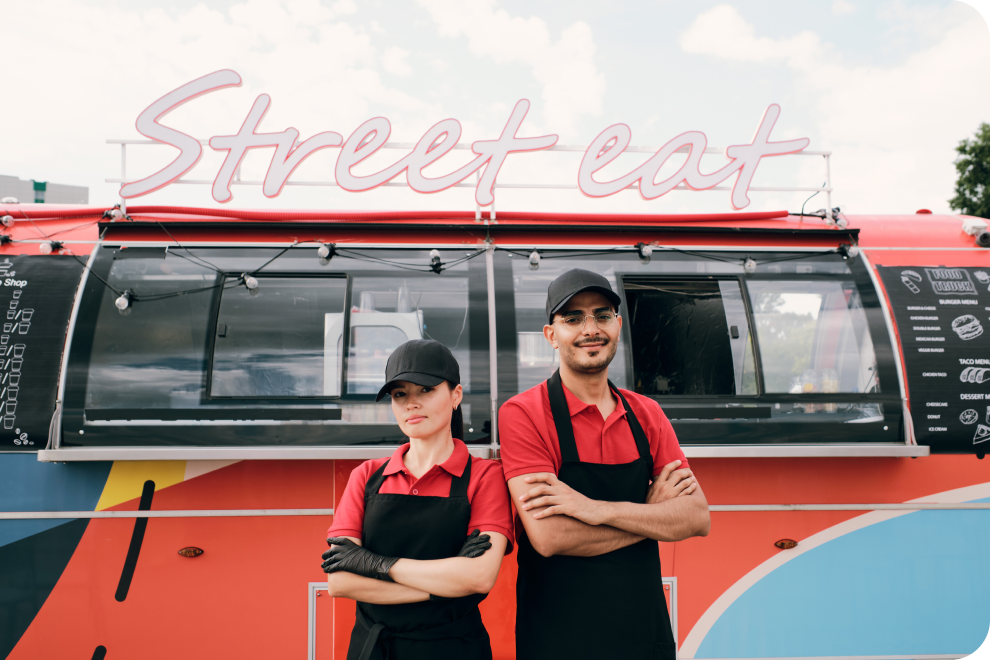 A male and female employee are standing in front of the food truck.