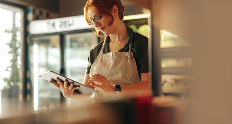 A female employee wearing an apron is using a tablet.