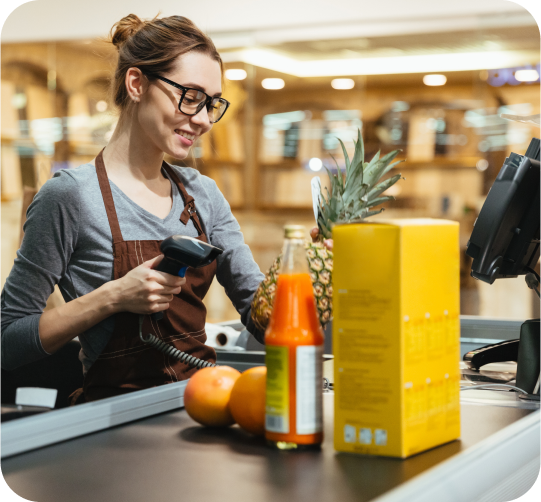 An employee of a convenience store is standing at the checkout counter and scanning products purchased by the customer.