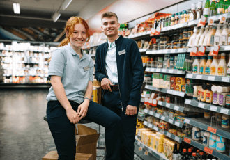 A female and male employee are standing in the grocery store.