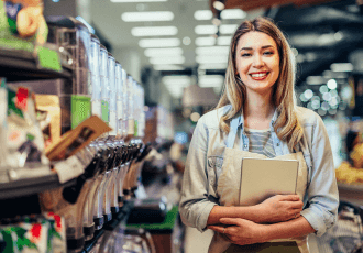 A female employee standing in the grocery store is holding a notepad.