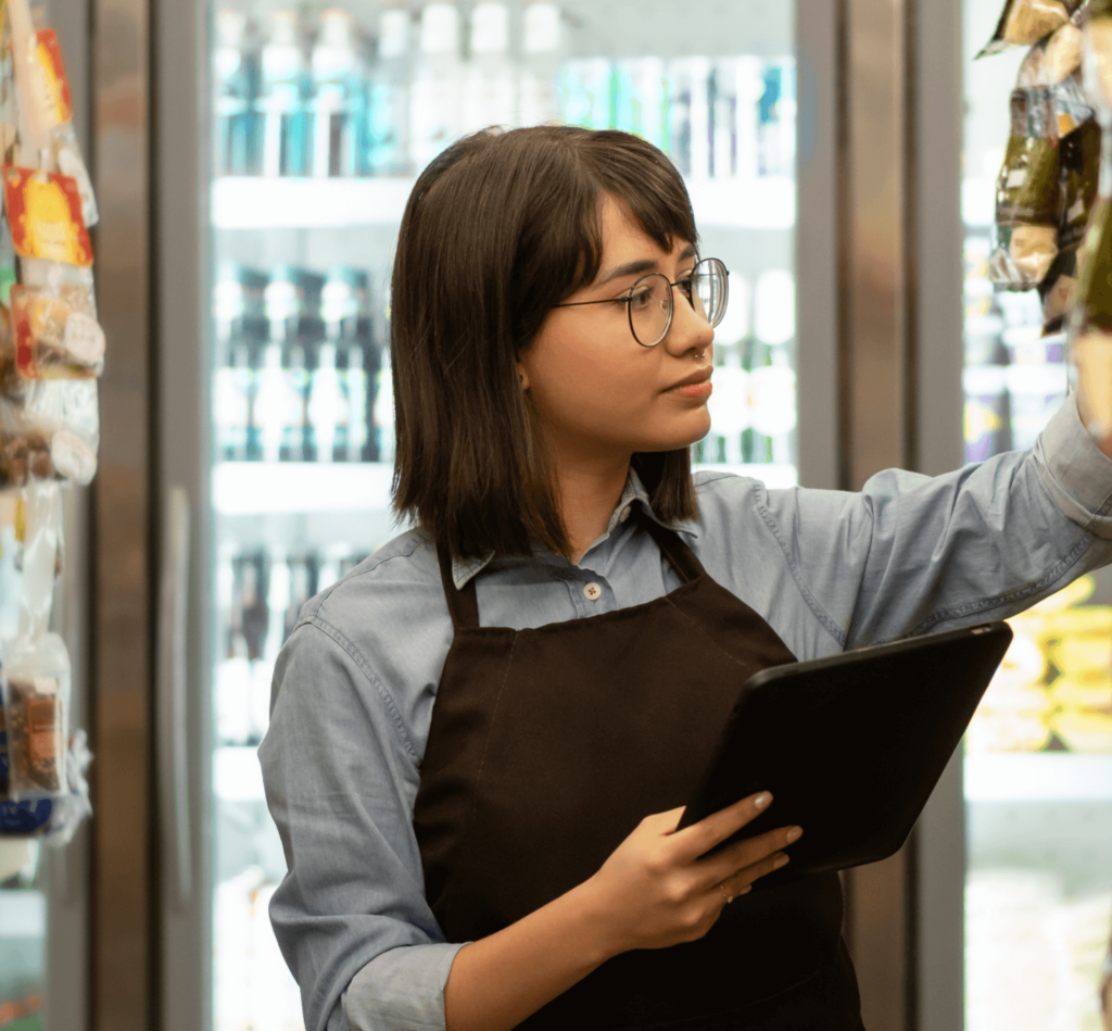 A female employee standing in the grocery store is holding a tablet and checking the inventory.