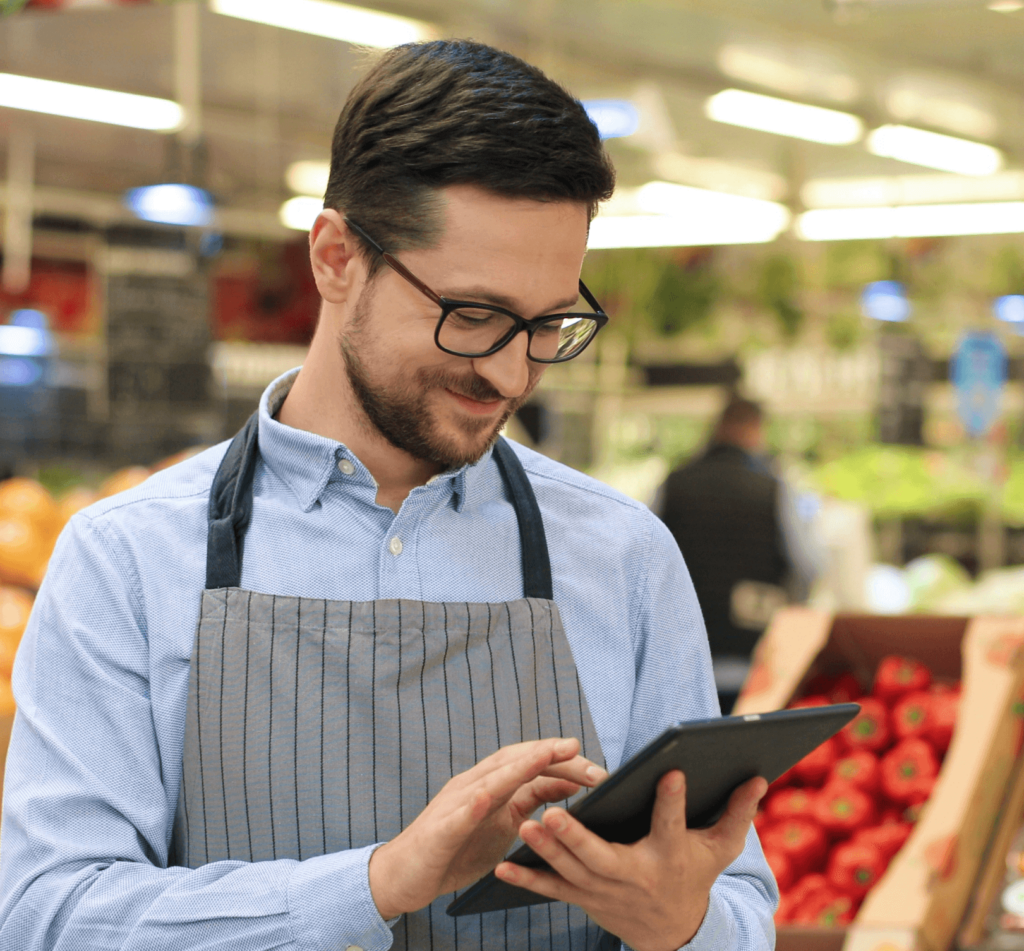 An employee standing in the grocery store is checking live sale updates on a tablet.