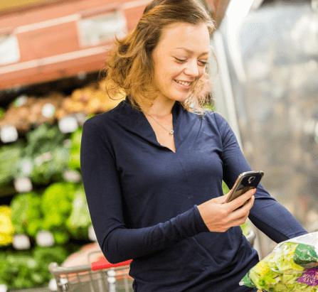 A woman standing in the grocery store is using a mobile.