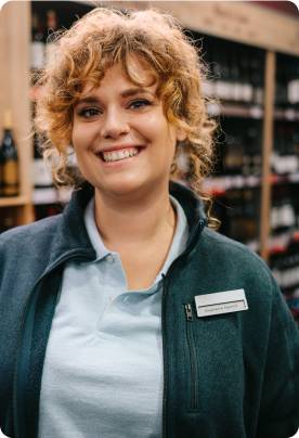A female employee standing in the liquor store is smiling.