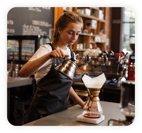 A female employee wearing an apron is pouring coffee in a jar.