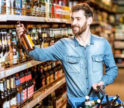 A man shopping for beer in a liquor store is putting a beer bottle in the hand basket.