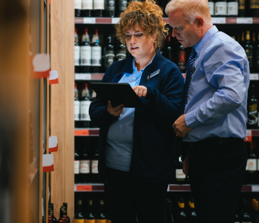 A female employee standing with a male employee in the liquor store is using the Modisoft POS system on the tablet.
