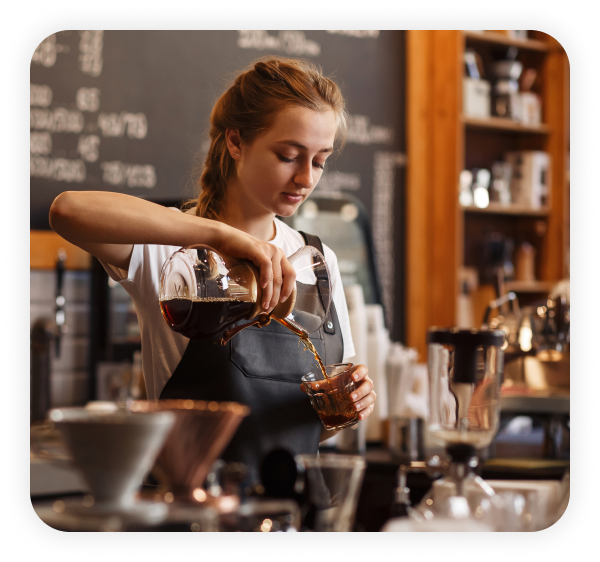 A female employee standing in a cafe is pouring coffee from a jar into a glass.