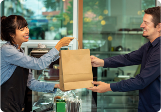 A female employee is giving paper bag to the male employee in the full service restaurant.