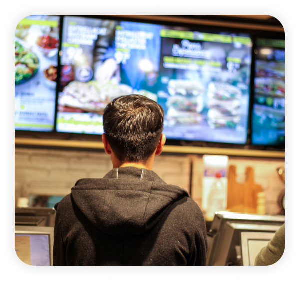 A boy standing in a restaurant is looking at the Modisoft digital menu board.