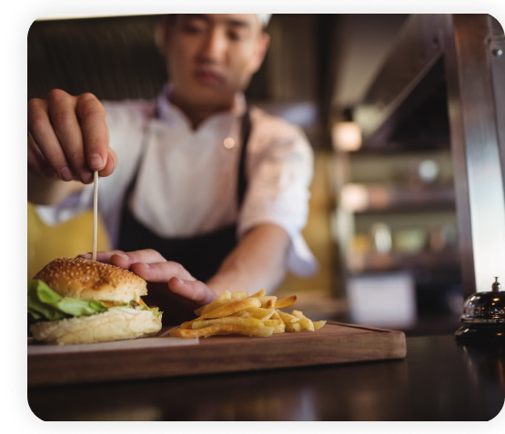 The chef standing in the kitchen is dressing and plating the burger.
