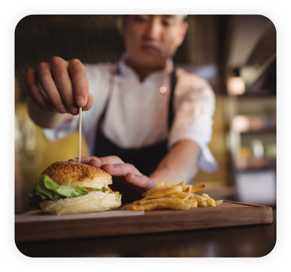 Chef is dressing the burger in the restaurant kitchen.
