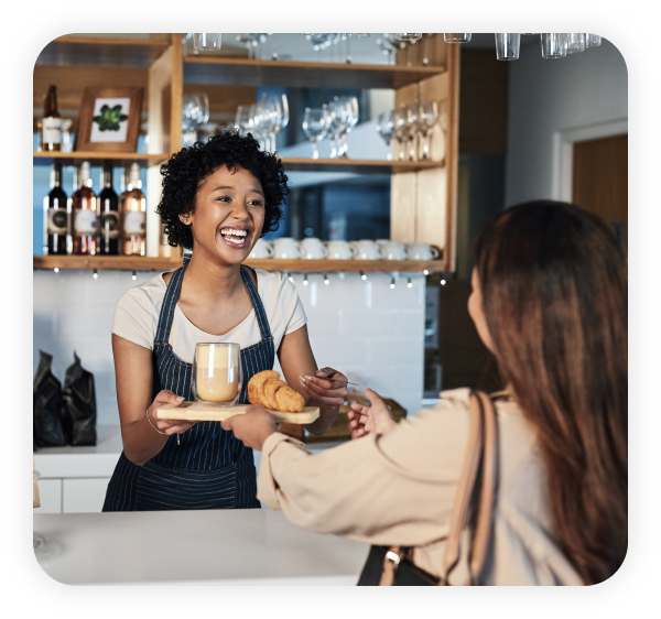A female employee wearing an apron is providing coffee and a loaf of bread to the female customer.