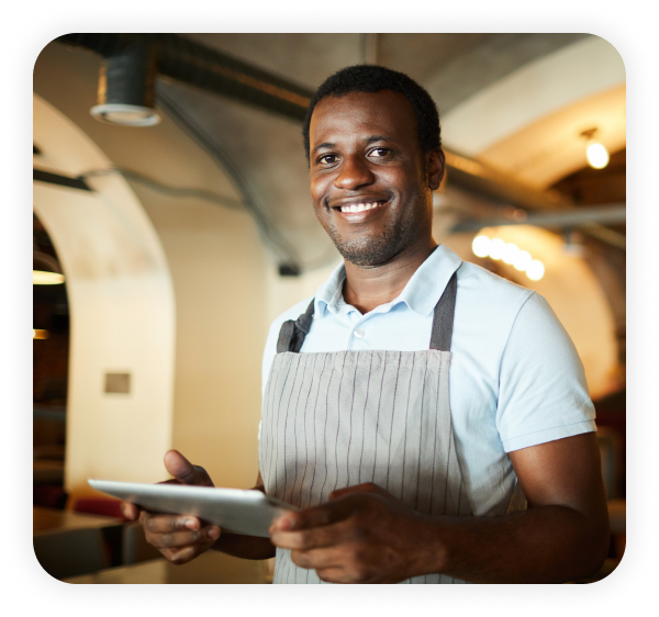A happy male employee wearing an apron is holding a tablet.