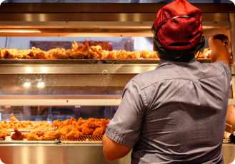 A male employee is taking chicken pieces from the counter to pack them for the customer.