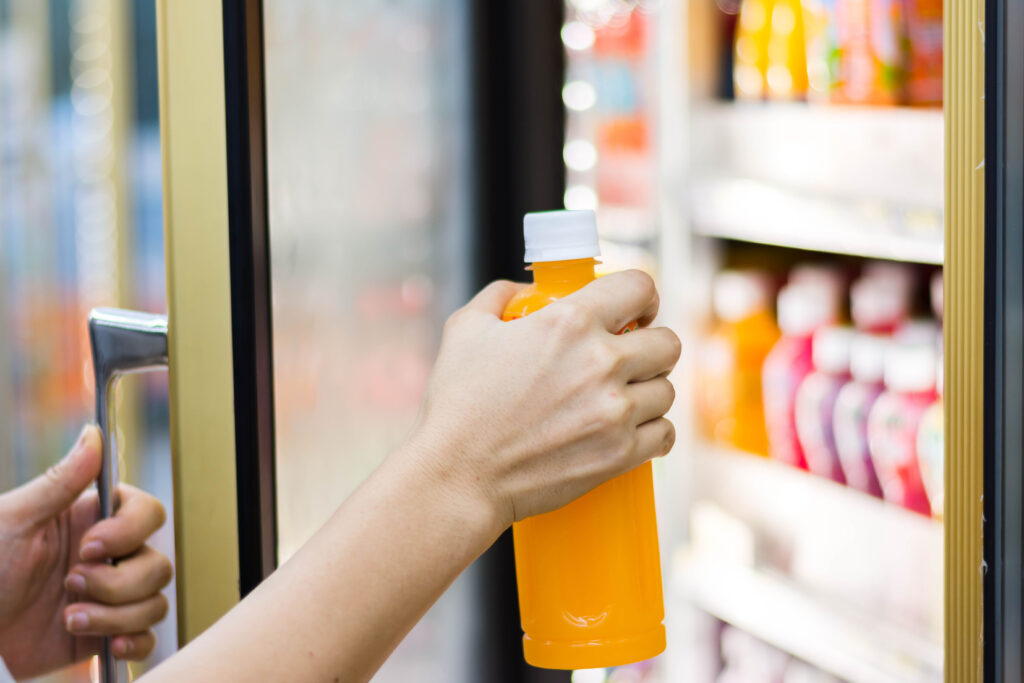 A customer is taking a juice bottle from the fridge of a convenience store.