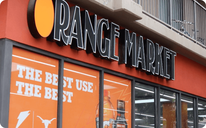 Orange Market storefront featuring branded exterior signage and convenience store window displays.