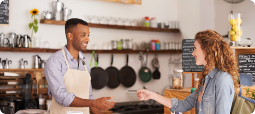 Store employee and customer exchanging a payment card at a retail counter, with shelves, cookware, and merchandise visible.