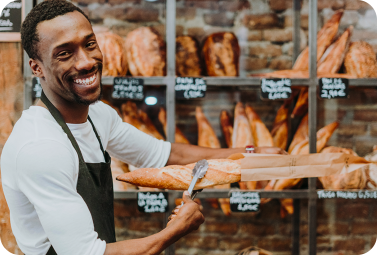 Bakery employee arranging freshly baked bread in front of artisan loaf displays and bakery shelving.