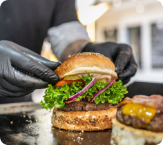 Food preparation scene showing a burger being assembled with lettuce, onions, and toppings.
