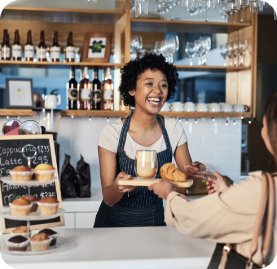 Cafe employee serving coffee and baked goods to a customer at a bakery counter.