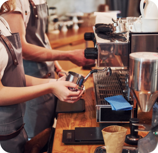 Cafe staff preparing beverages at an espresso machine station with coffee equipment and preparation tools.