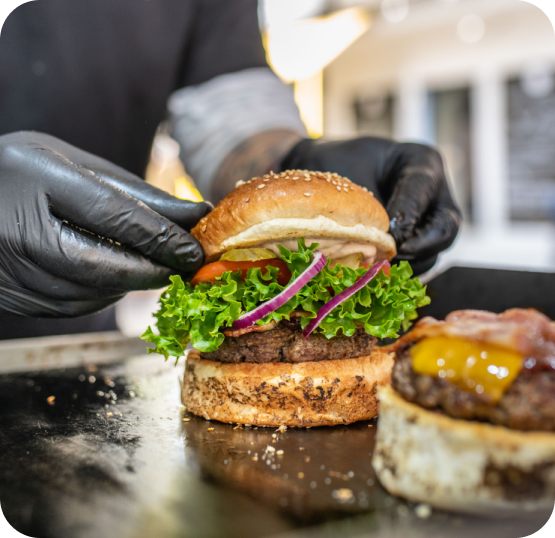 Food service staff assembling burgers with fresh toppings at a fast casual food preparation station.