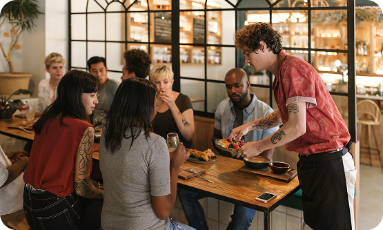 Food and beverage service setting with guests seated at a table while a server delivers plated meals.