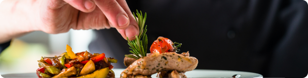 Hand garnishing a plated dish with fresh herbs during food presentation and preparation.