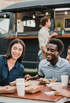 Guests enjoying meals and beverages at an outdoor dining table beside a food truck.