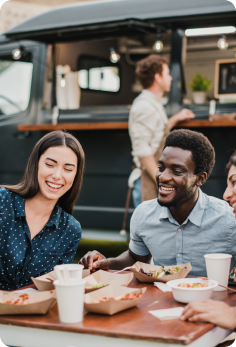 Guests enjoying meals and beverages at an outdoor dining table beside a food truck.