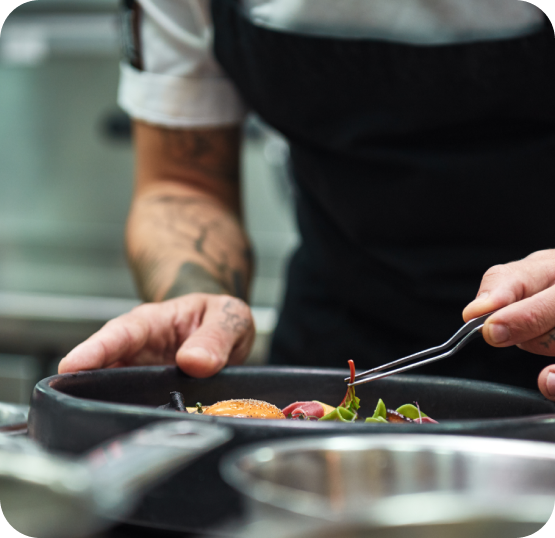 Kitchen staff carefully plating and garnishing a prepared dish during service in a full-service restaurant kitchen.