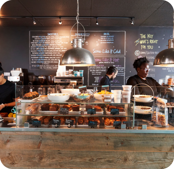 Cafe and bakery display counter featuring pastries, baked goods, beverage equipment, and menu boards in a food service environment.
