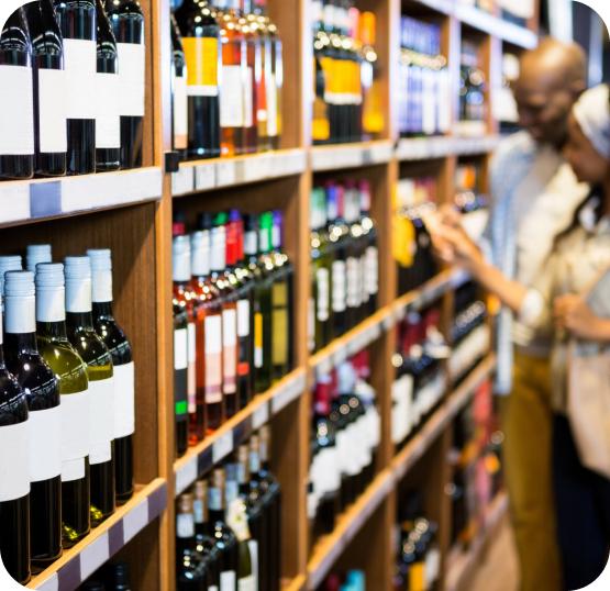 Retail shelving displaying wine and bottled beverage products with customers browsing product selections in the background.