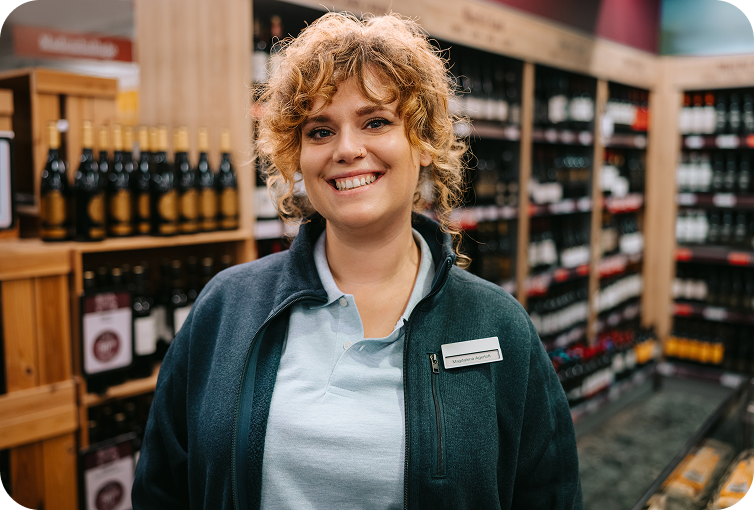 Store employee standing in a liquor store aisle surrounded by wine and beverage shelves, highlighting product organization and inventory management.