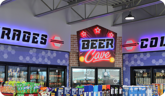 Convenience store beverage section featuring refrigerated coolers, packaged products, and illuminated in-store signage.