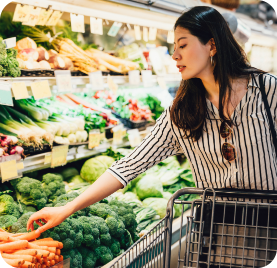 Customer selecting fresh produce from a grocery store display while shopping with a grocery cart.